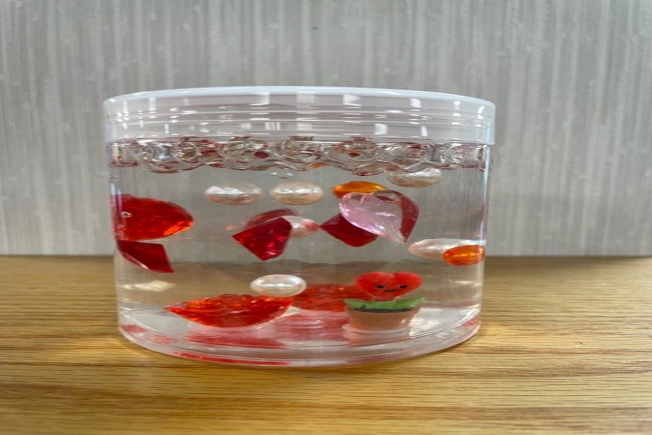 a round, plastic container with plastic flowers and hearts floating in water