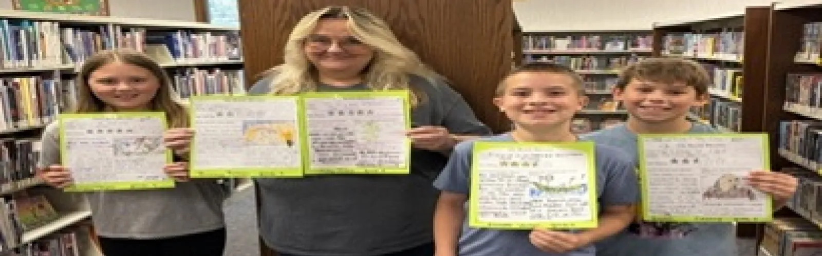 three fourth grade students display their book reviews while the children's librarian holds two other reviews