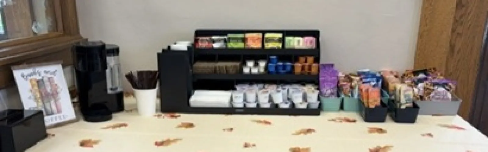table set with a Keurig, travel cups, creamers, sugar, tea bags and  variety of snacks