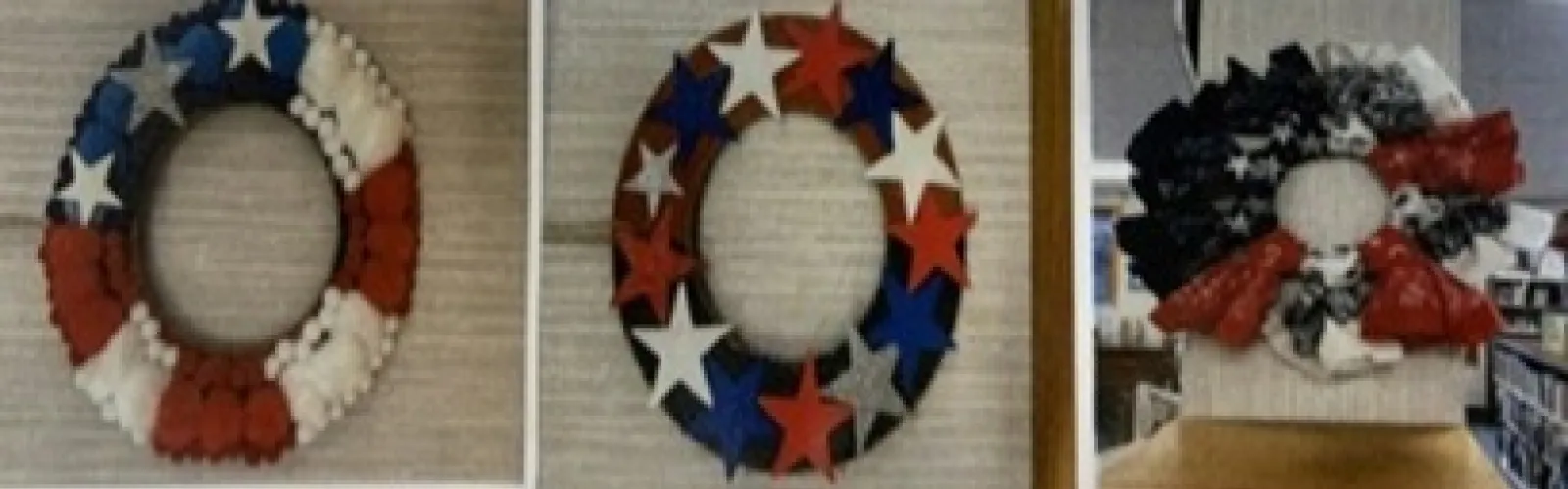 A cardboard circle decorated with pom-poms to resemble an American flag, a cardboard circle decorated with red, white, blue and silver stars, and a wreath created from bandanas to resemble an American flag